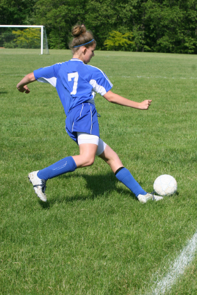 Teenage female soccer player kicking ball
