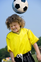 Young soccer player closing his eyes while heading ball